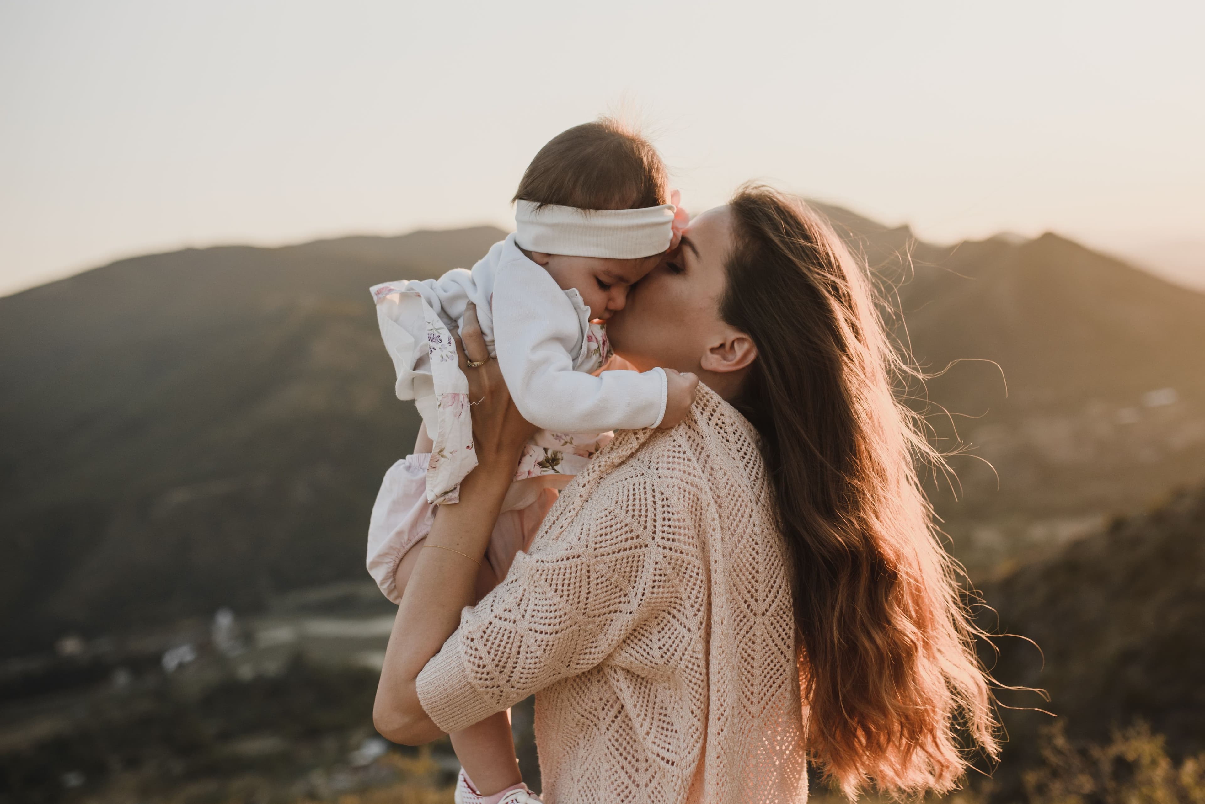 Mãe erguendo e beijando o bebê contra a luz do fim do dia
